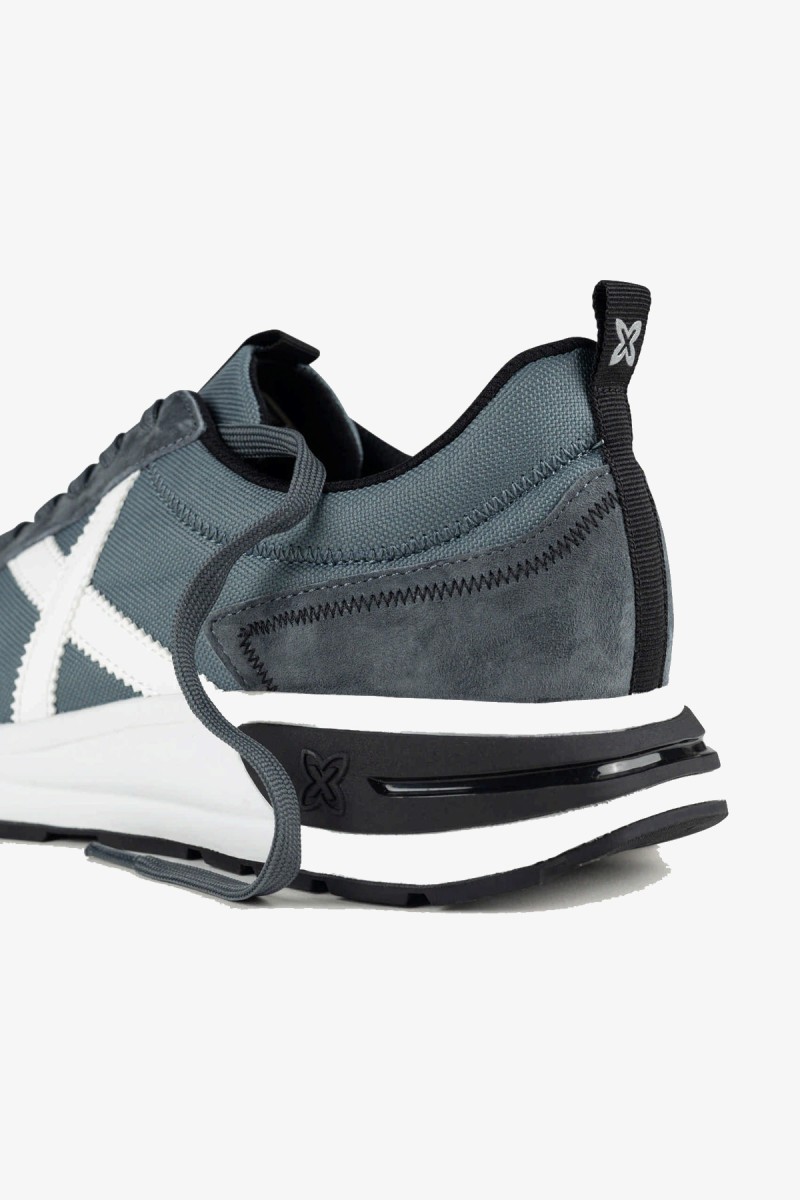  Zapatillas Munich de inspiración running de los años 80 con una estética urbana y casual. Su combinación de gris azulado y blanco aporta un estilo deportivo, sobrio y fácil de integrar en los looks diarios. 